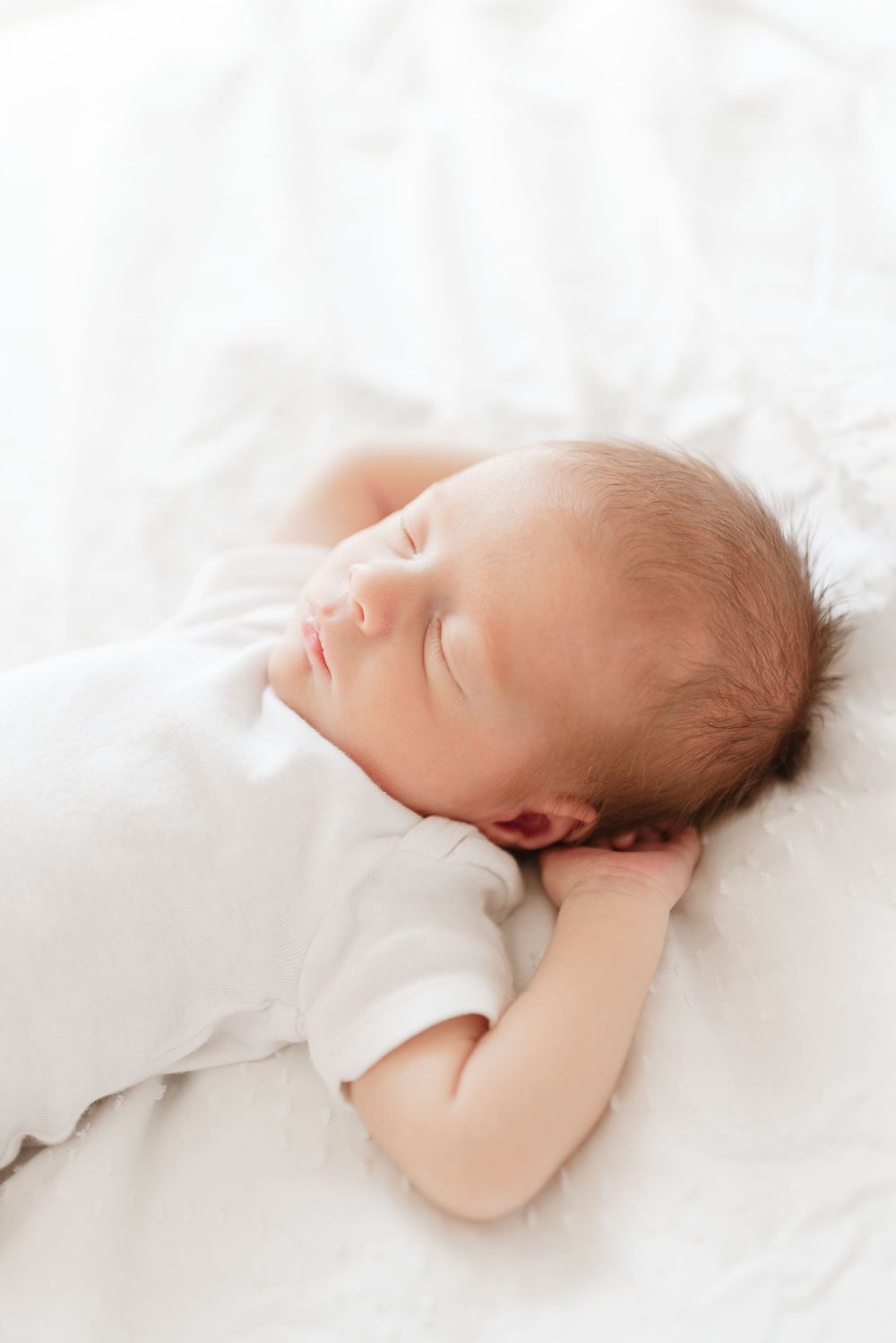 Soft image of newborn baby napping in bed during a newborn photo session in Toronto home, captured by Jess GC Photography