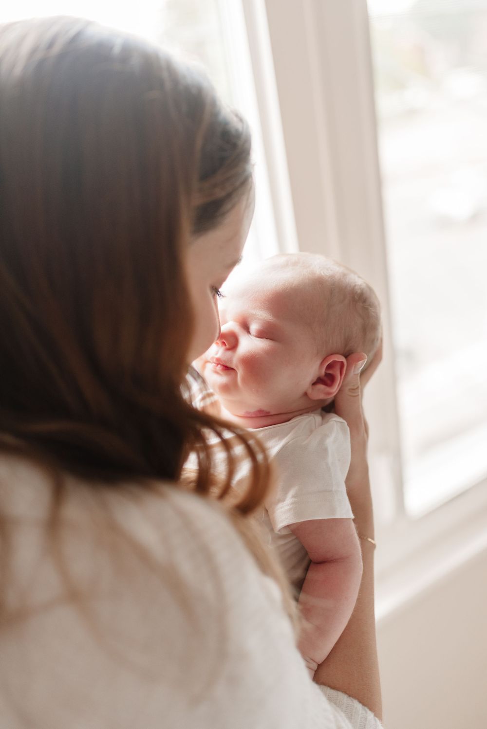 Mother and baby touching nose by window for a lifestyle newborn photography session in Toronto home, captured by Jess GC Photography