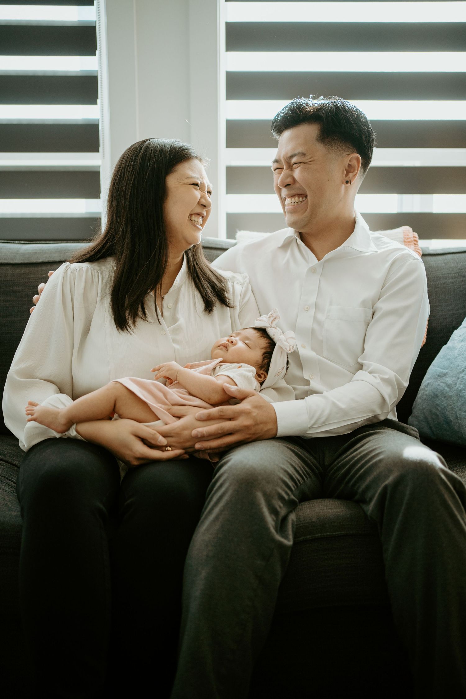 Happy couple shares a joyful moment with their newborn baby while sitting on a dark couch at home.