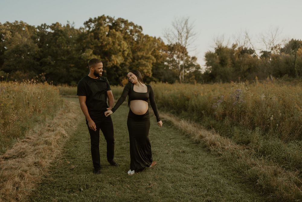 A couple walks together on a dirt path through a golden field at sunset creating a romantic silhouette.