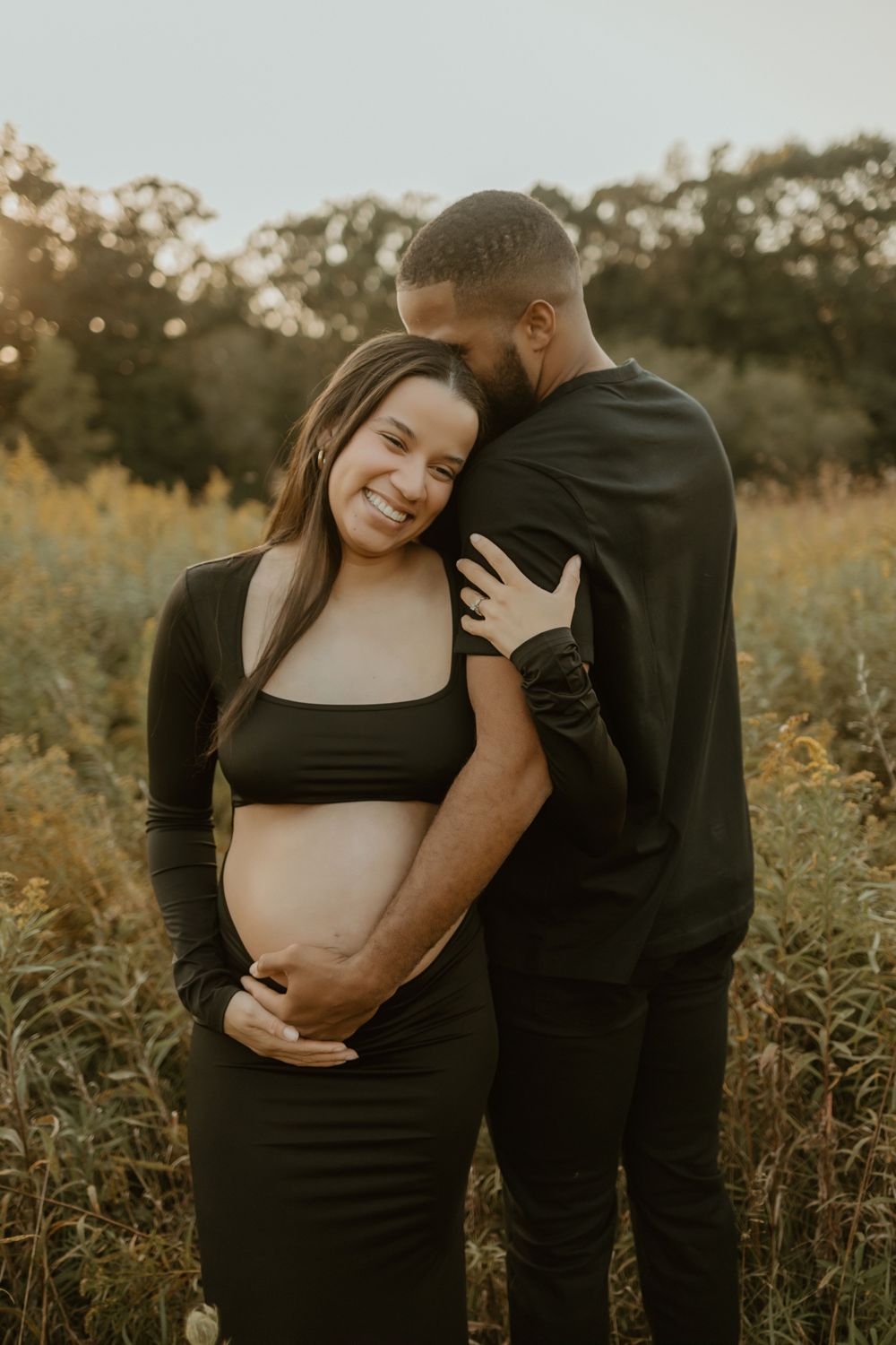 Intimate maternity photoshoot in a golden field at sunset showing tender moments between expecting couple.