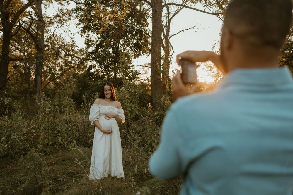 A maternity photo session in a wooded area with soft natural lighting filtering through the trees.