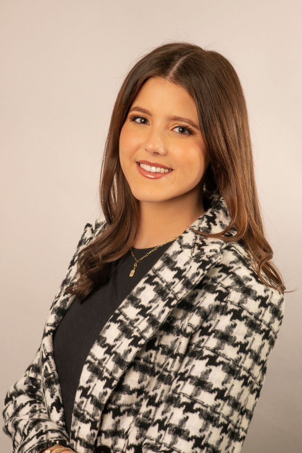 Professional portrait showing a person in a black and white houndstooth blazer with long brown hair and a warm smile.