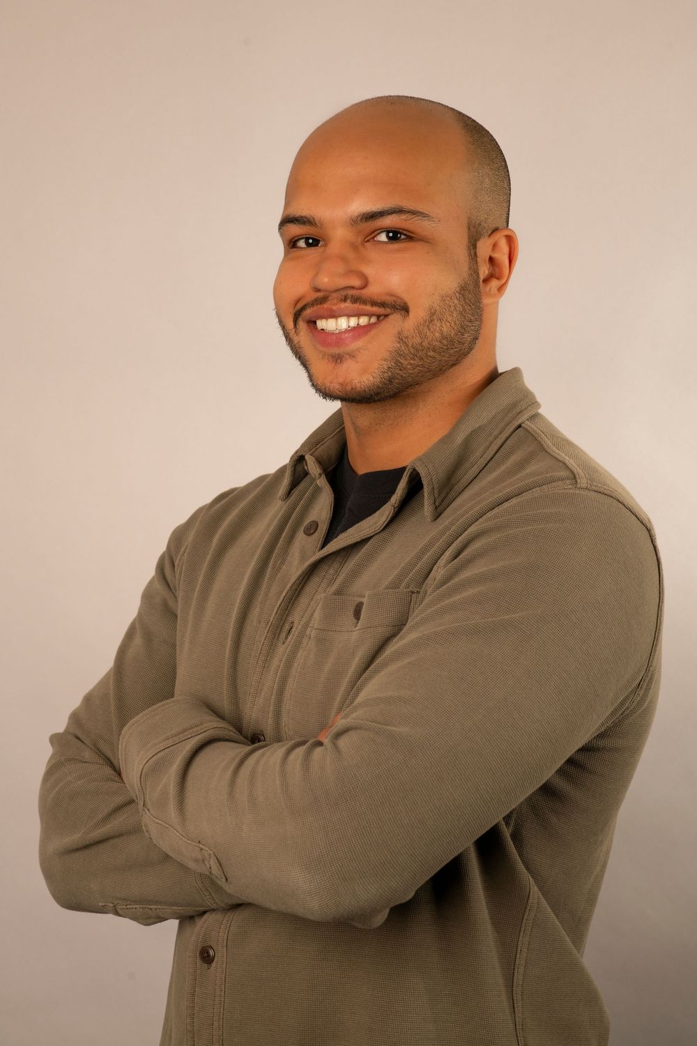 Professional headshot of a smiling person wearing an olive-colored button-up shirt against a neutral background.