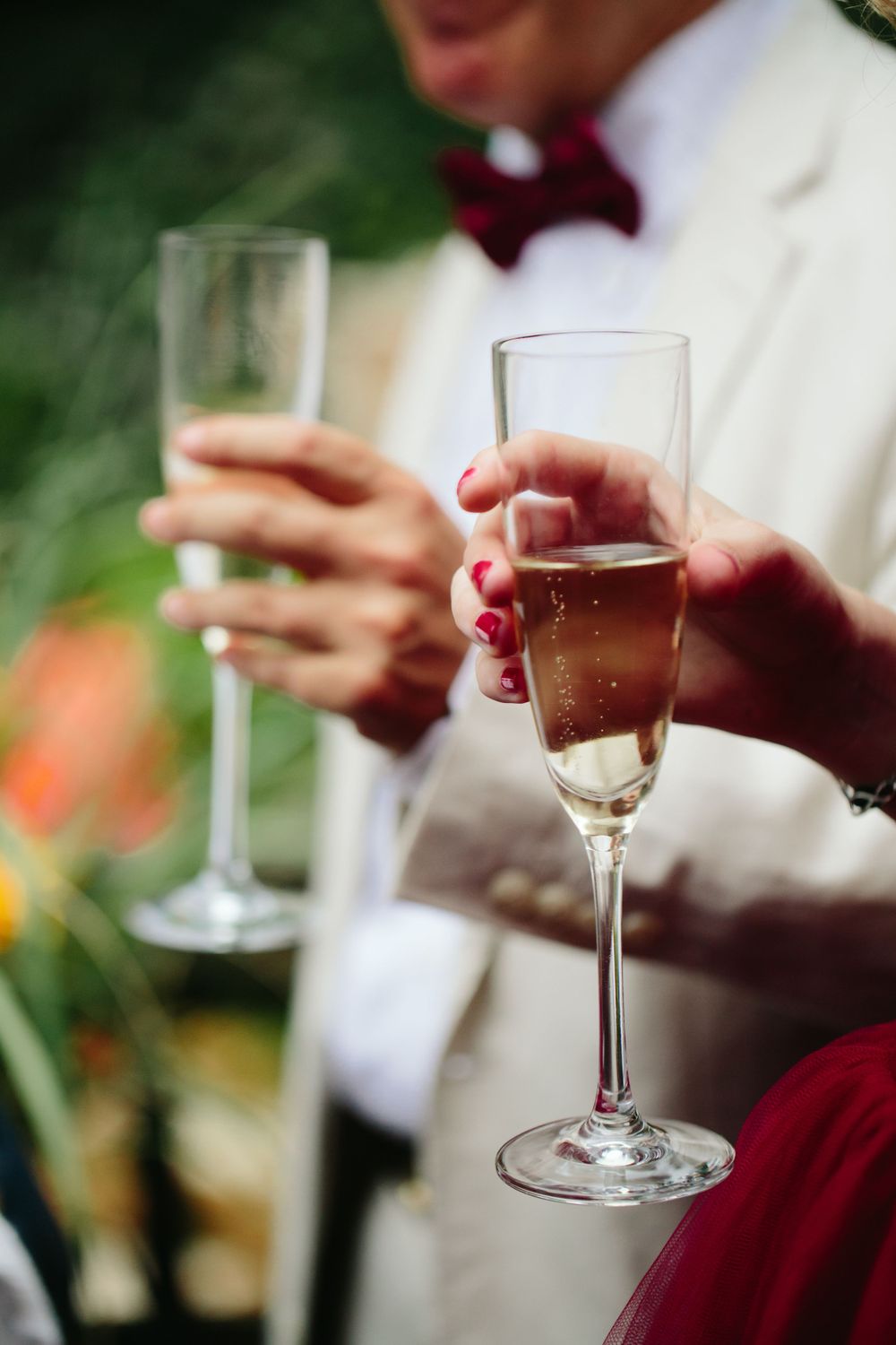 Two champagne flutes held by hands in formal attire at a backyard garden wedding celebration.