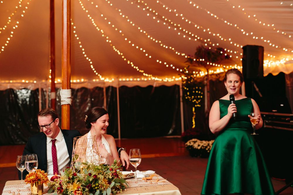 Bride and groom laughing at hilarious maid of honor toast under the tent at the historic Pierce House in Lincoln, MA