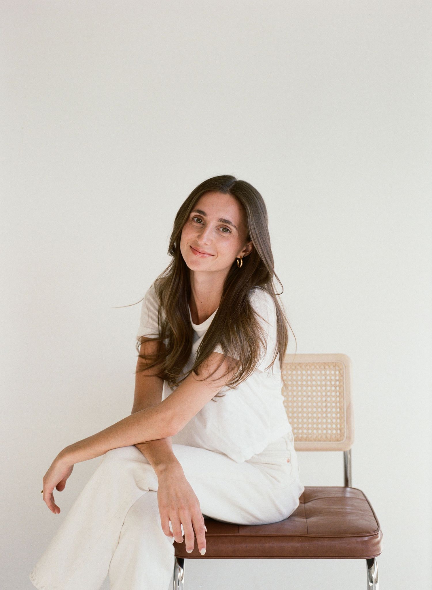 A portrait in natural light shows someone in casual black and white attire seated against a minimal background.