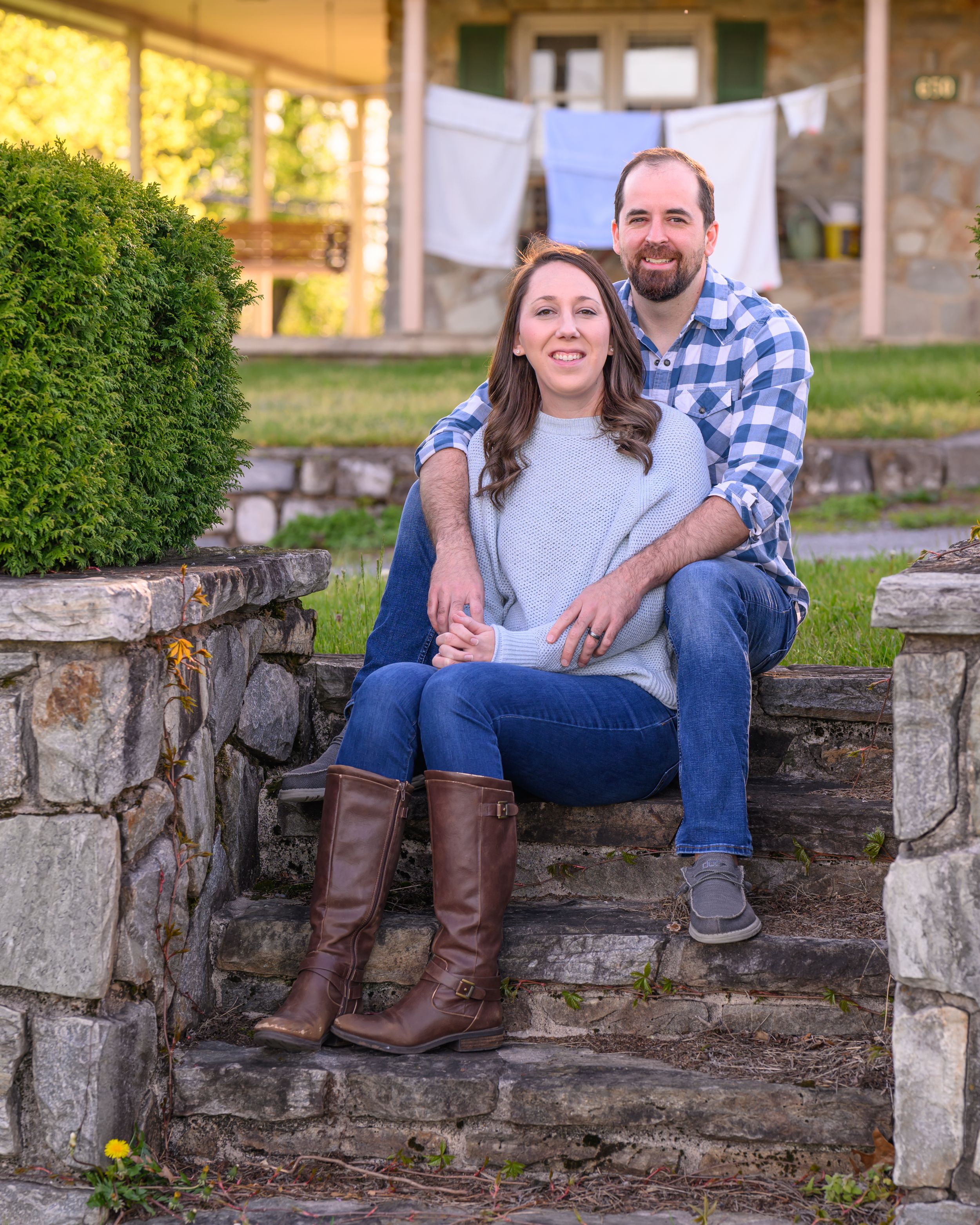 A couple sits together on stone steps outdoors with laundry hanging on a clothesline in the background during sunset.