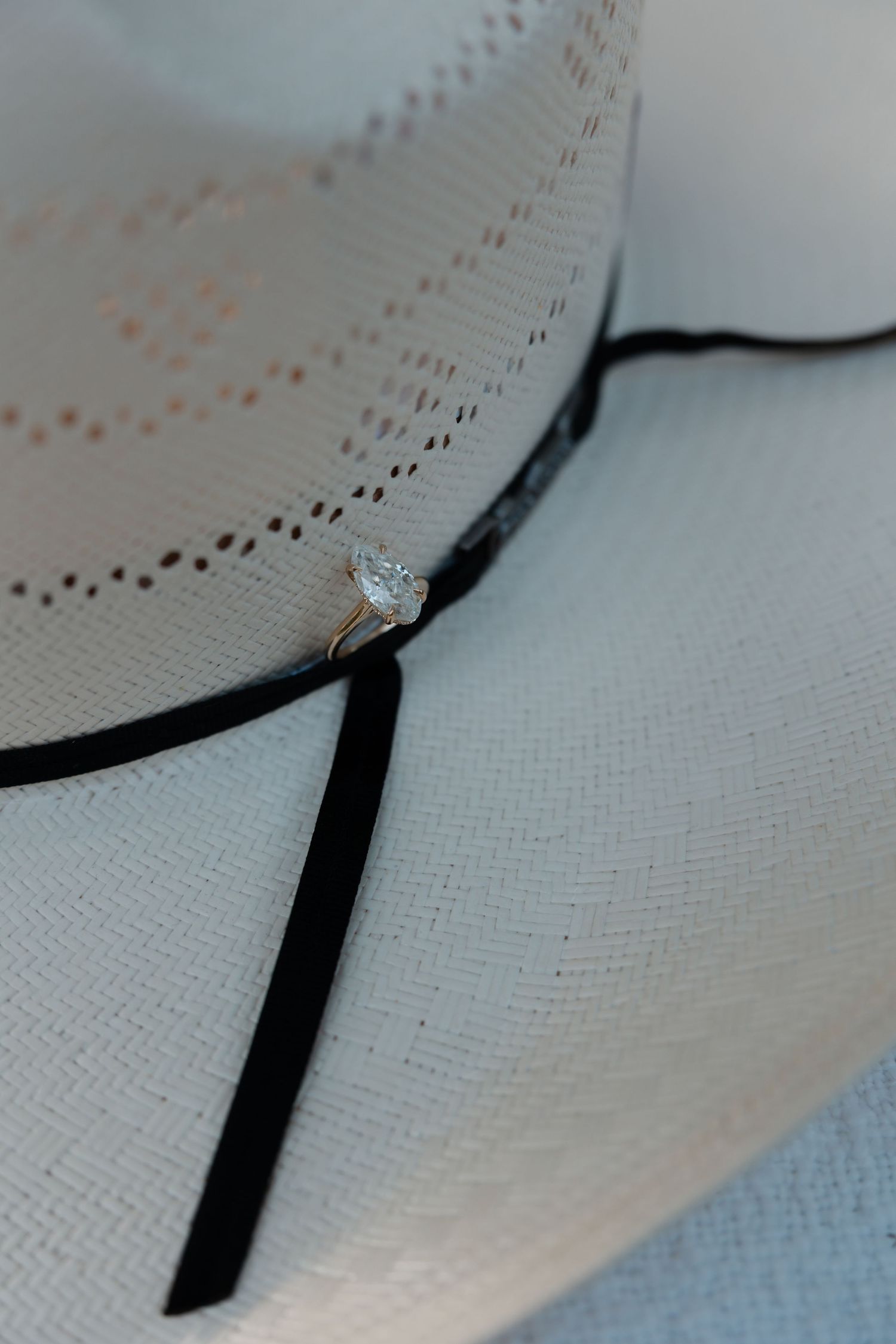 Diamond engagement ring resting on brim of white straw cowboy hat with black band.