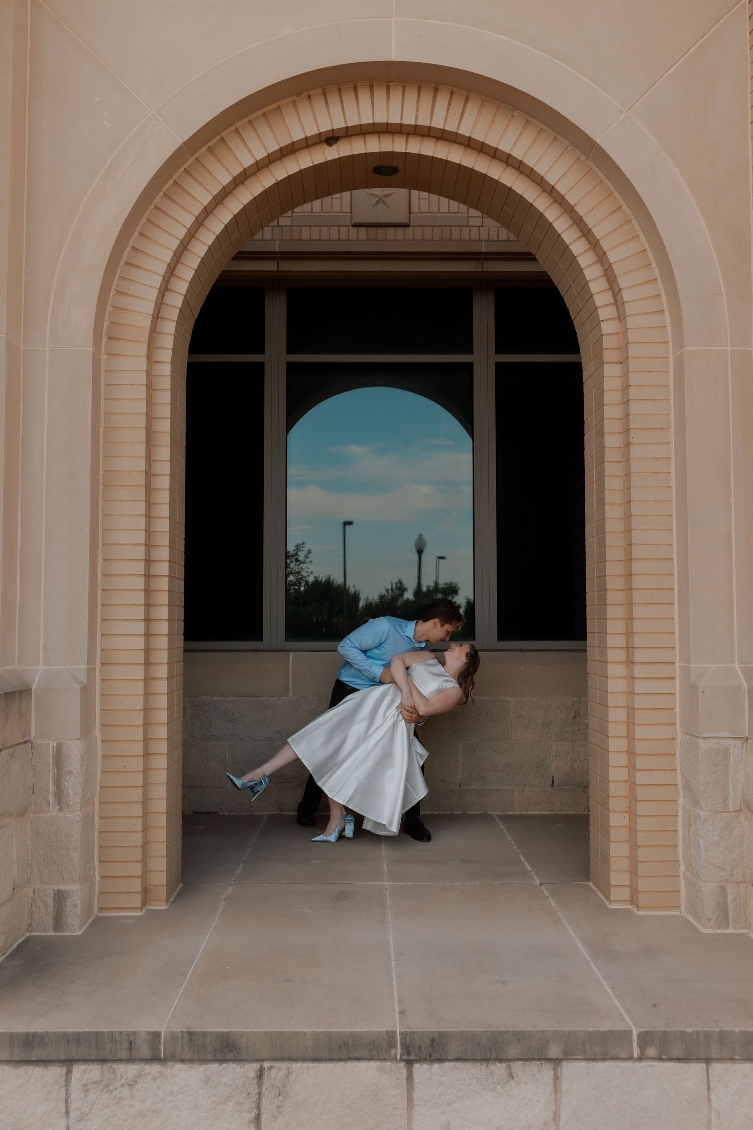 Couple sharing a romantic dip kiss under an elegant brick archway during their wedding photo session.