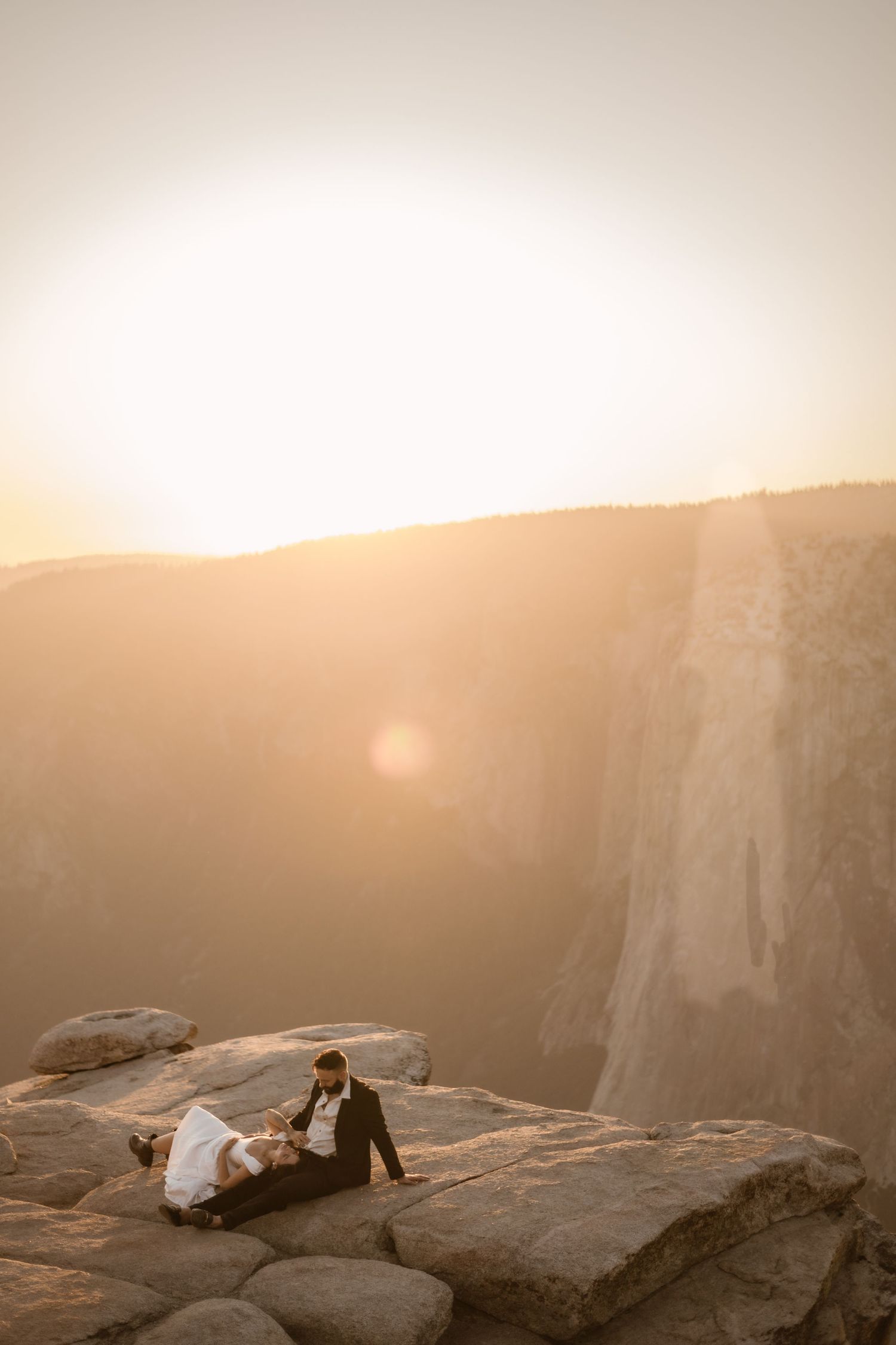 Silhouette of a couple standing on cliff edge at Yosemite during golden hour sunset.