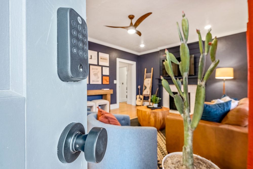 Interior view of a modern living room with a smart lock, cactus plant, and orange furniture accents.