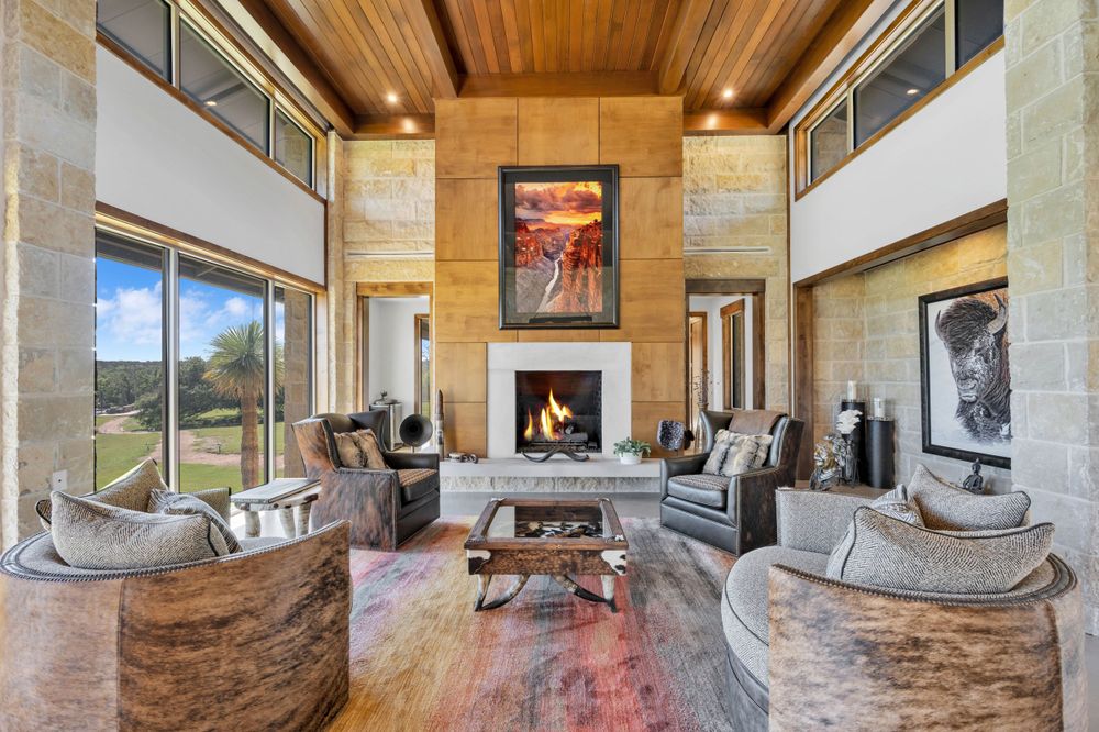 Modern luxury living room with high wood ceiling, stone fireplace, and grey curved sofas in an open concept space.