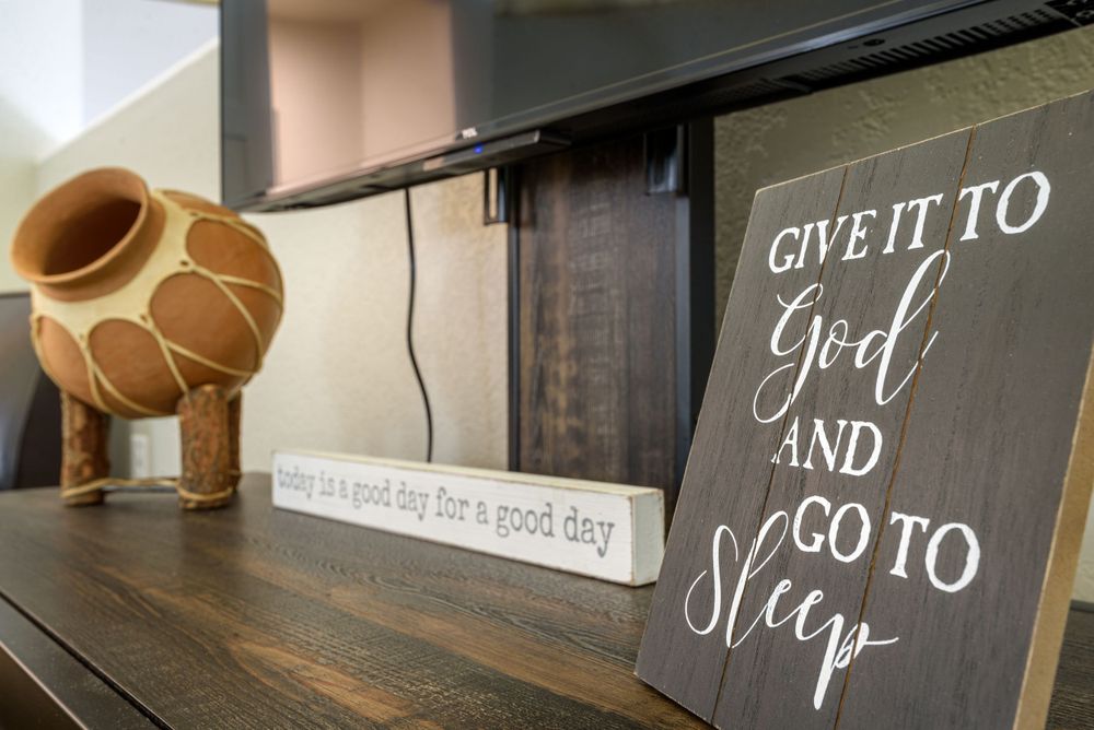 A decorative wooden sign reading 'Give It To God And Go To Sleep' displayed on a dark shelf with a ceramic vase nearby.