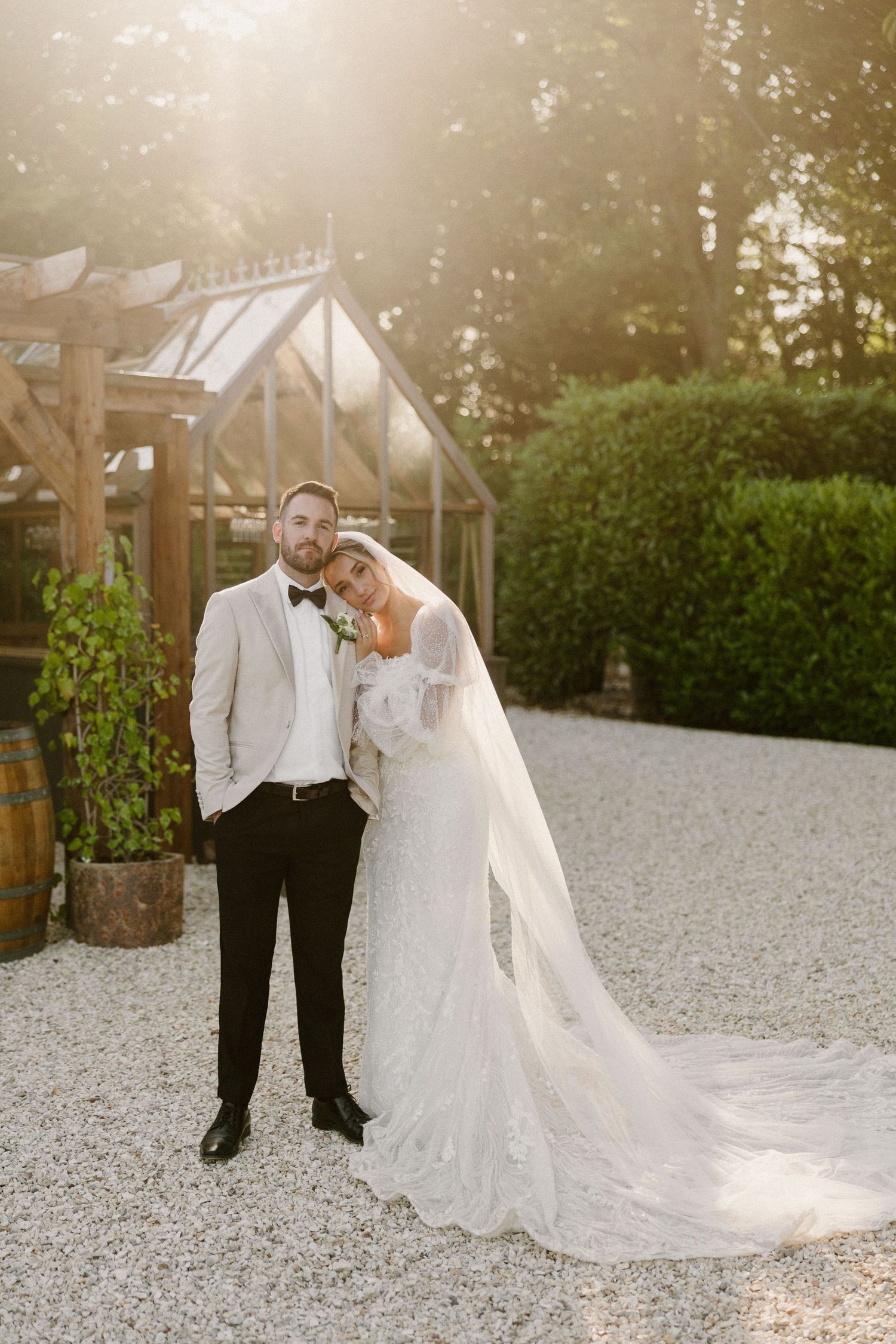 Couple in wedding attire walking on a stone path surrounded by countryside scenery.