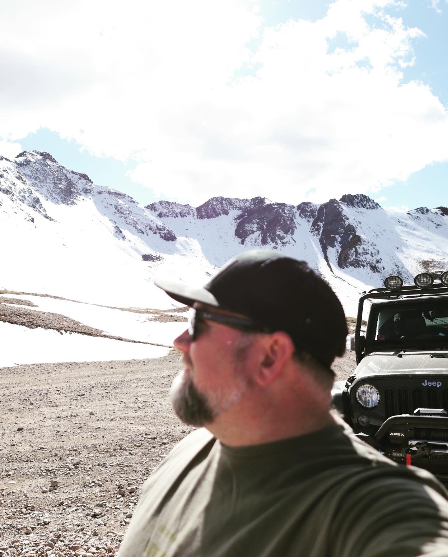A mountain landscape with a vehicle silhouetted against snow-capped peaks in rugged terrain.