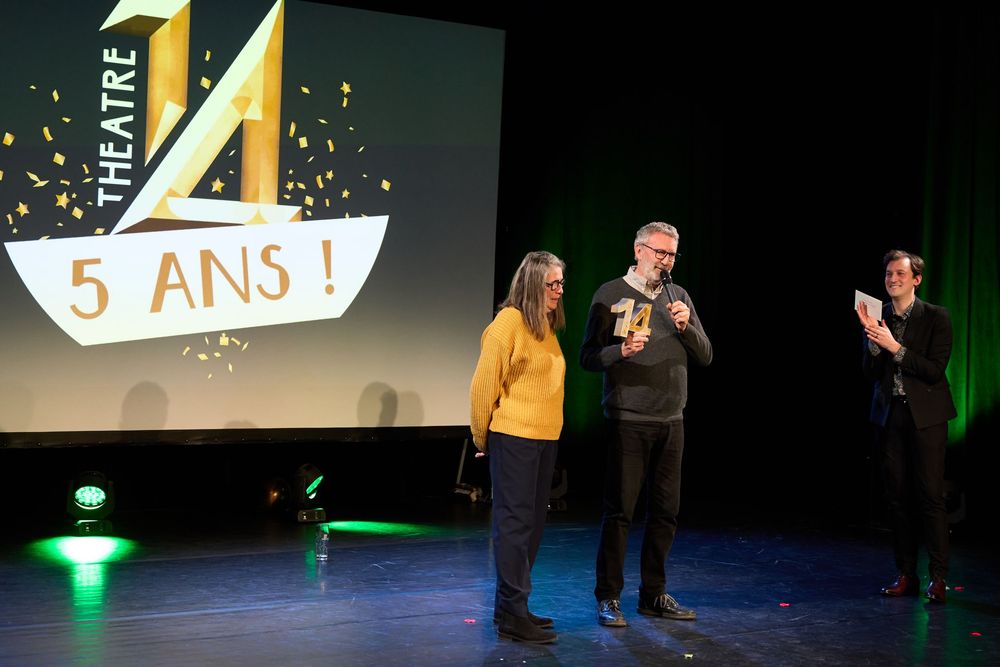 A theater stage with performers celebrating a 5-year anniversary with a yellow logo projection in the background.
