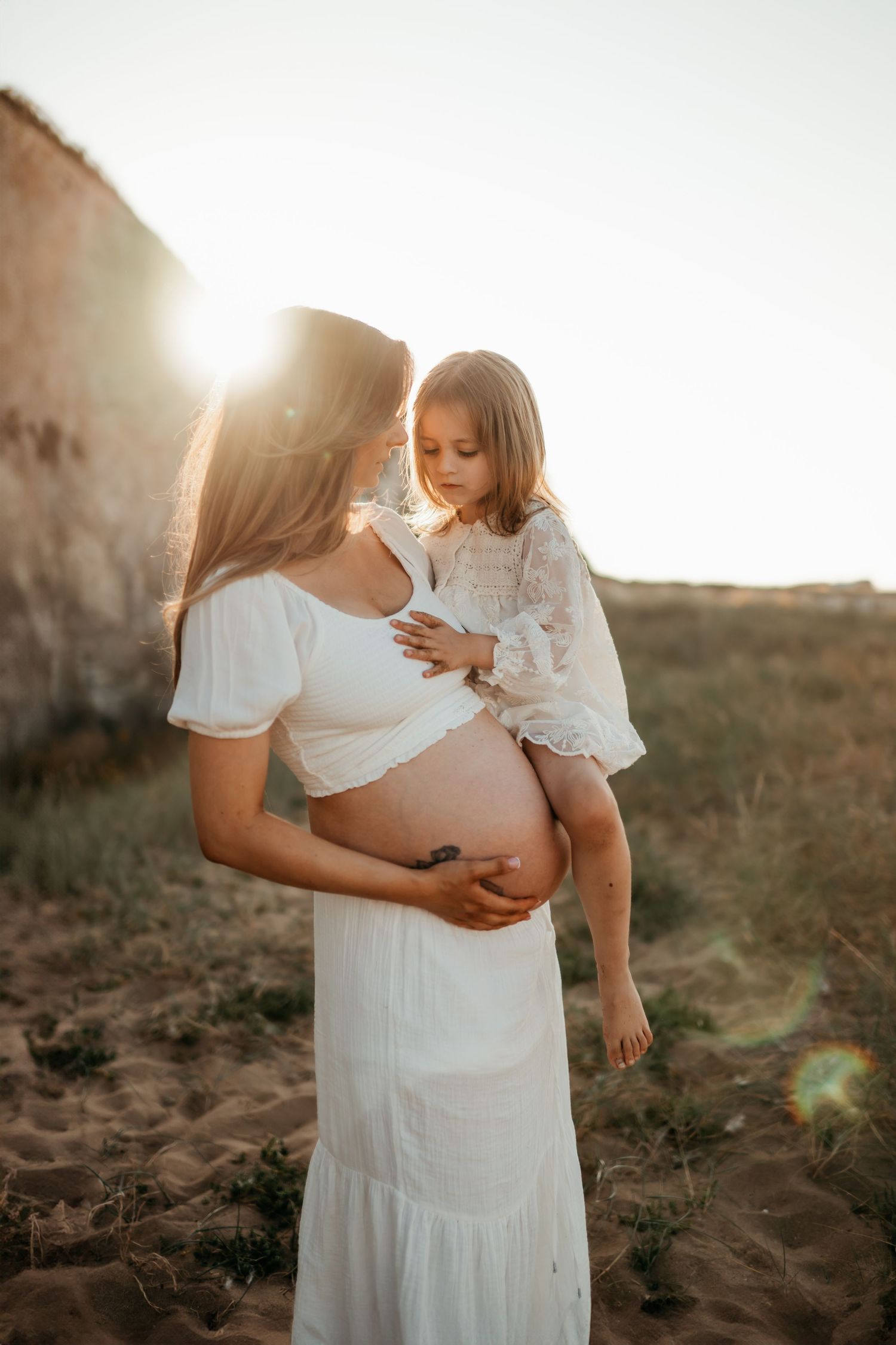 A pregnant mother holding her daughter at sunset in Botany Bay, Kent family Photographer