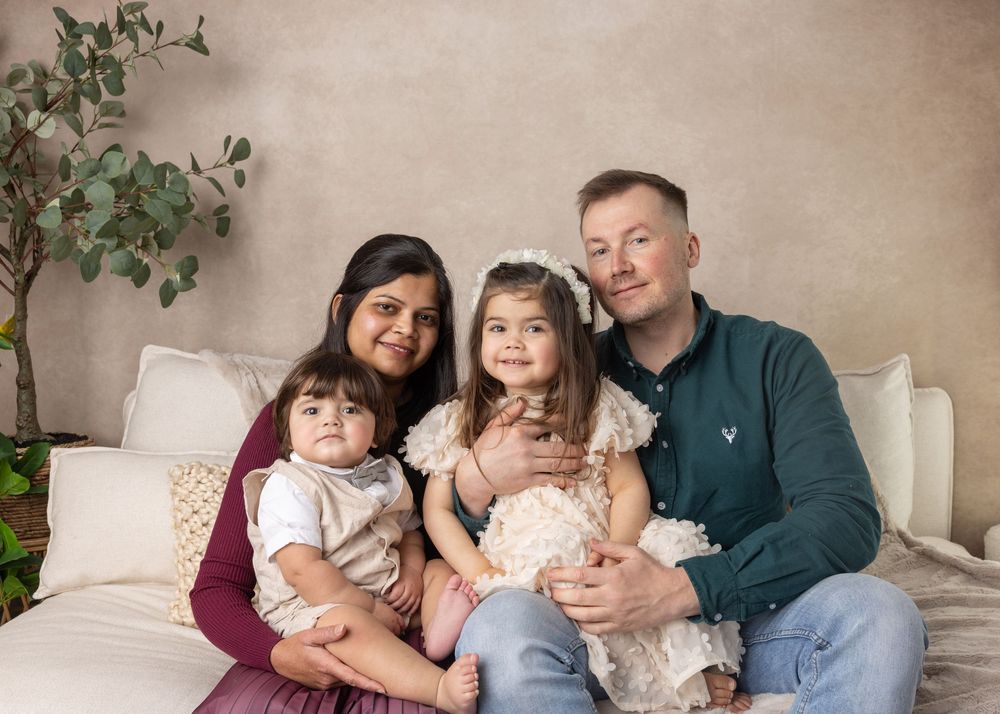 A family lounging together in casual attire on a beige sofa with green plants in the background.