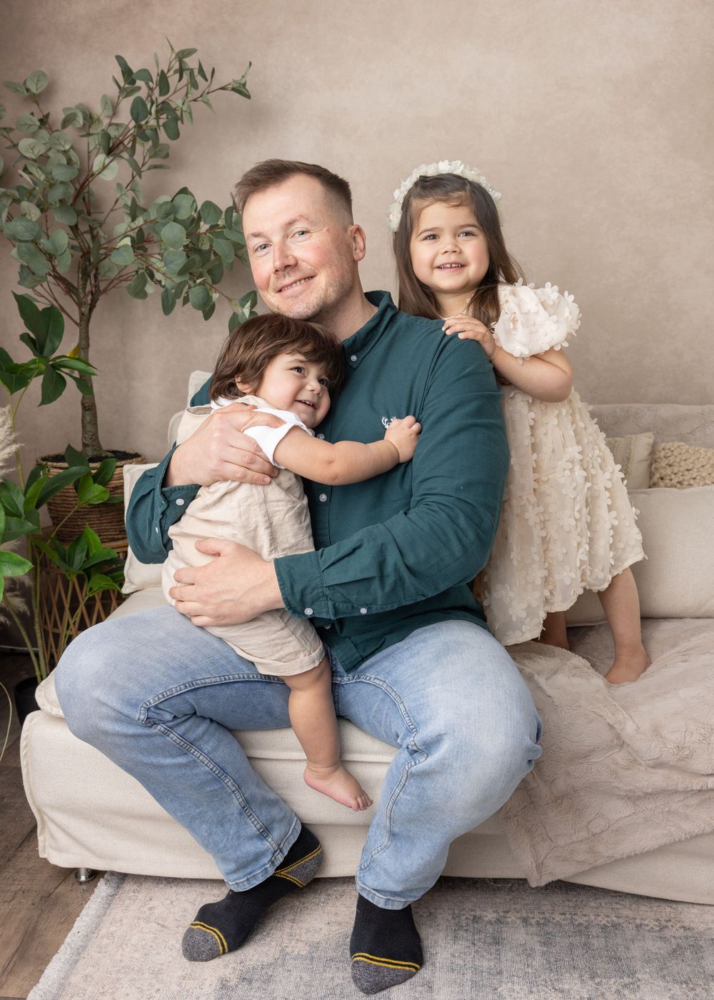 A family portrait shows a dad in teal shirt with two children sitting on a beige couch with a decorative plant nearby.