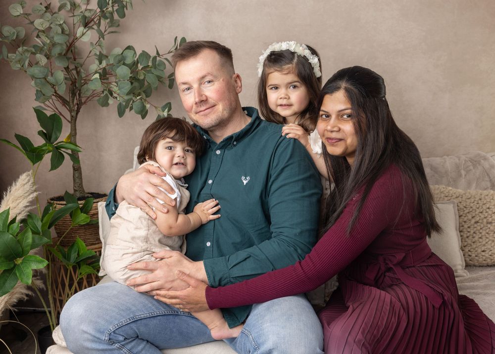 A family in coordinating dark green and burgundy outfits sits together on a couch during a photo session.