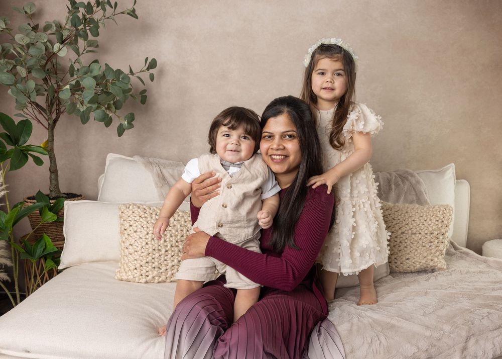 Family sitting together on white couch with decorative pillows and green plant in corner.