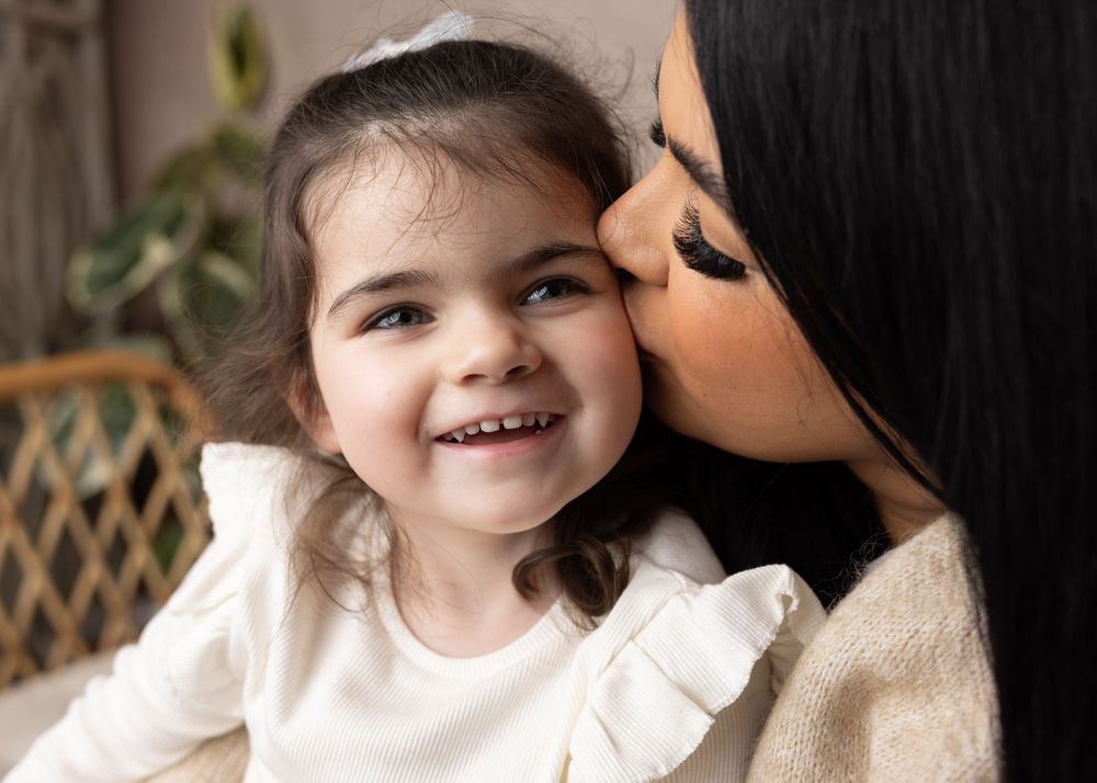 A touching moment of affection and joy between a parent and young child wearing white, both smiling warmly.