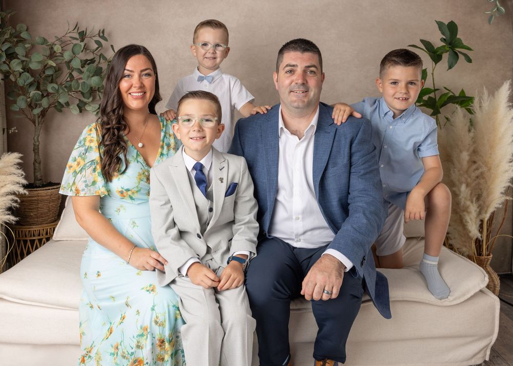Family portrait on beige sofa wearing coordinated blue and floral outfits in a studio setting.
