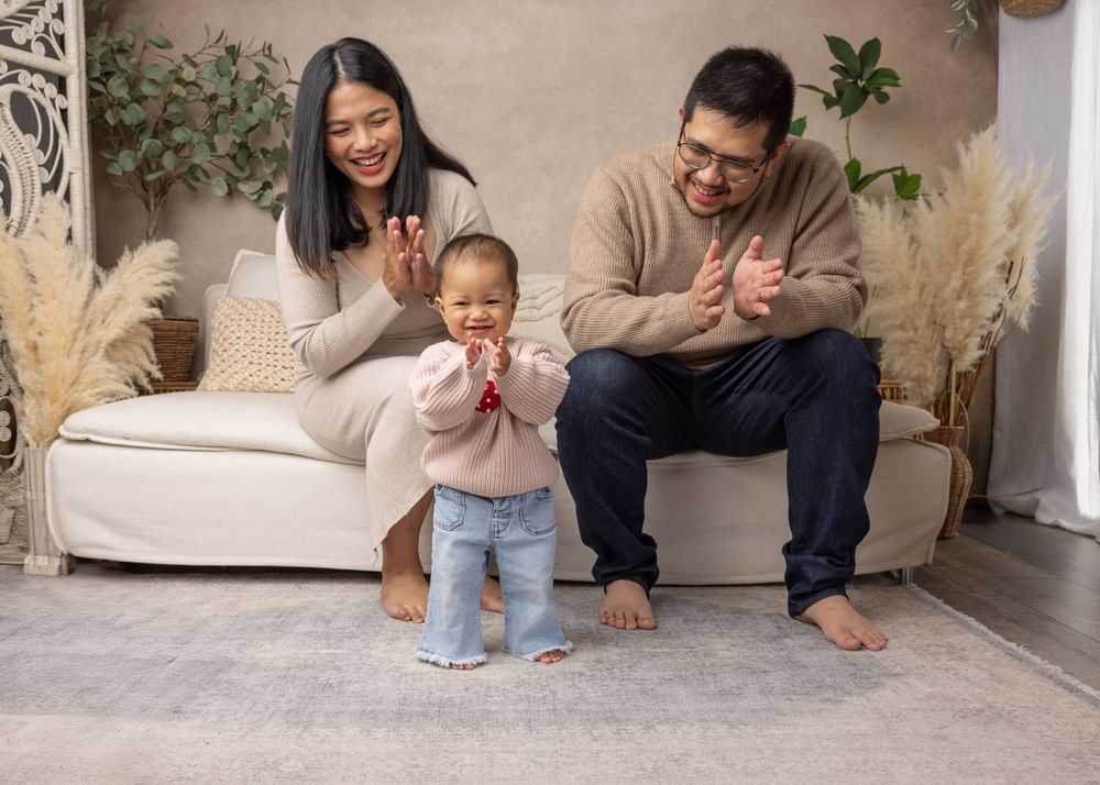 Family enjoying playful moment together on beige sofa with pampas grass decor and plants in background.