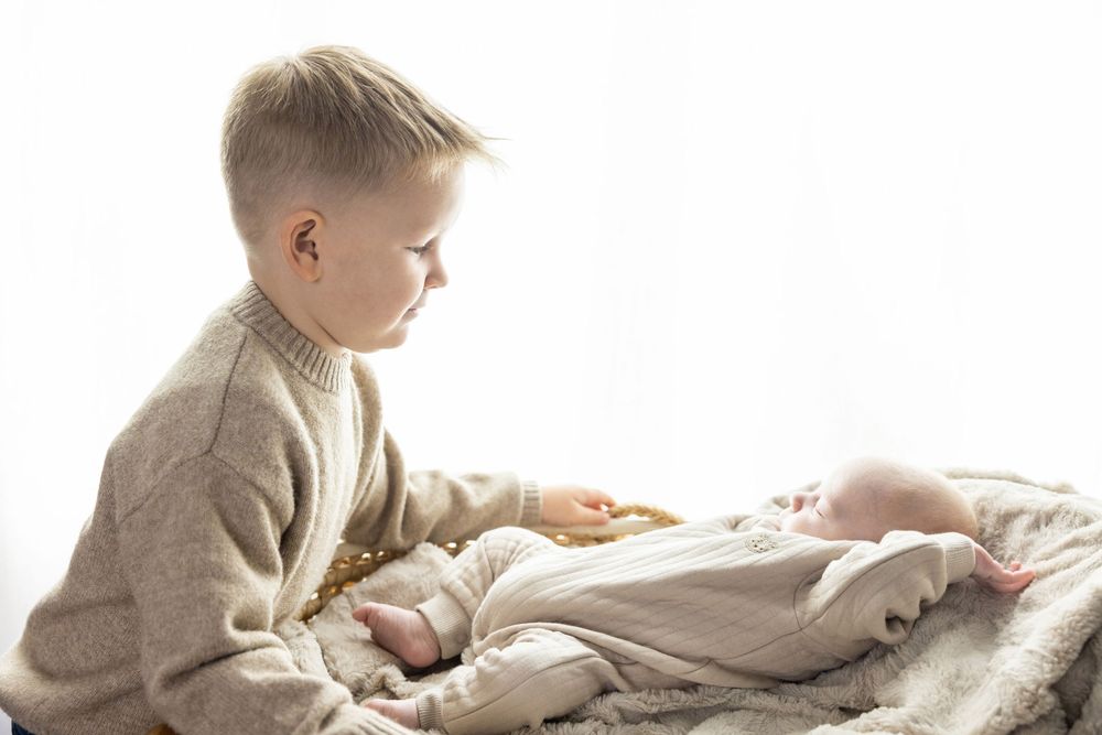 Two children reading books together while relaxing on white bedding in natural light.