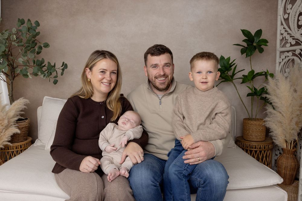 Family sitting together on a beige couch with indoor plants decorating the background.