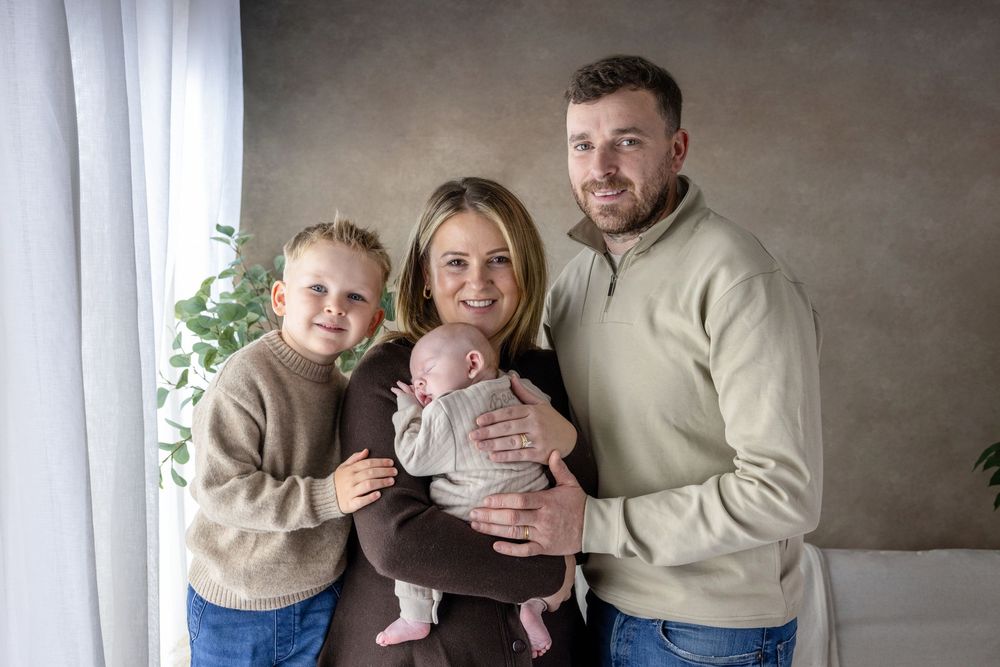 A family wearing coordinated beige sweaters poses together for a casual indoor photo shoot.