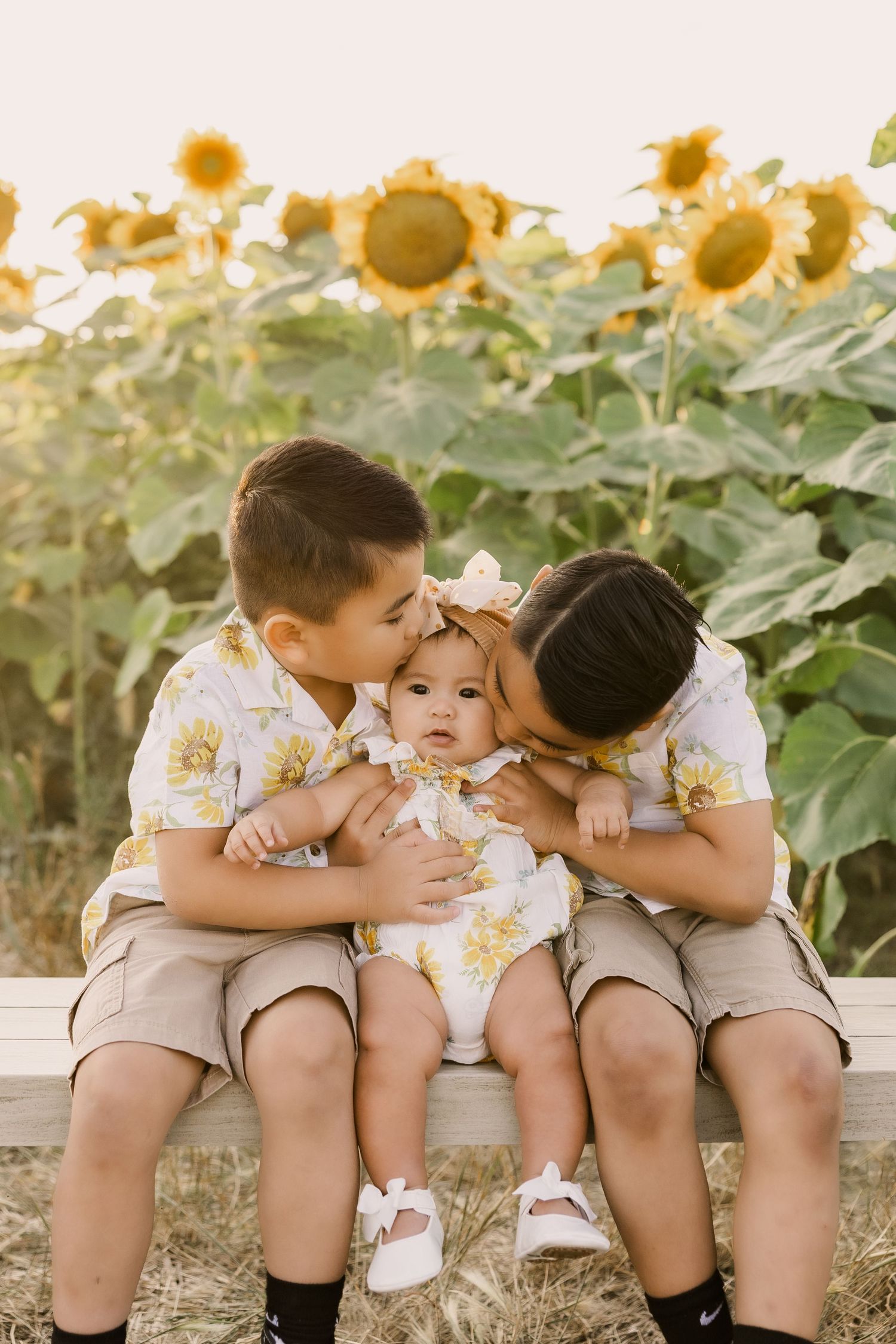 A happy baby in a peach-colored dress sits on a striped blanket outdoors.