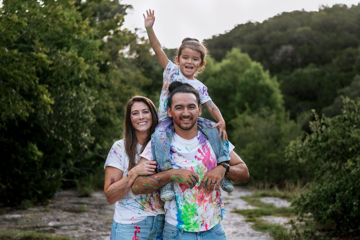 Group in colorful paint-splattered clothing having fun during outdoor color powder celebration.