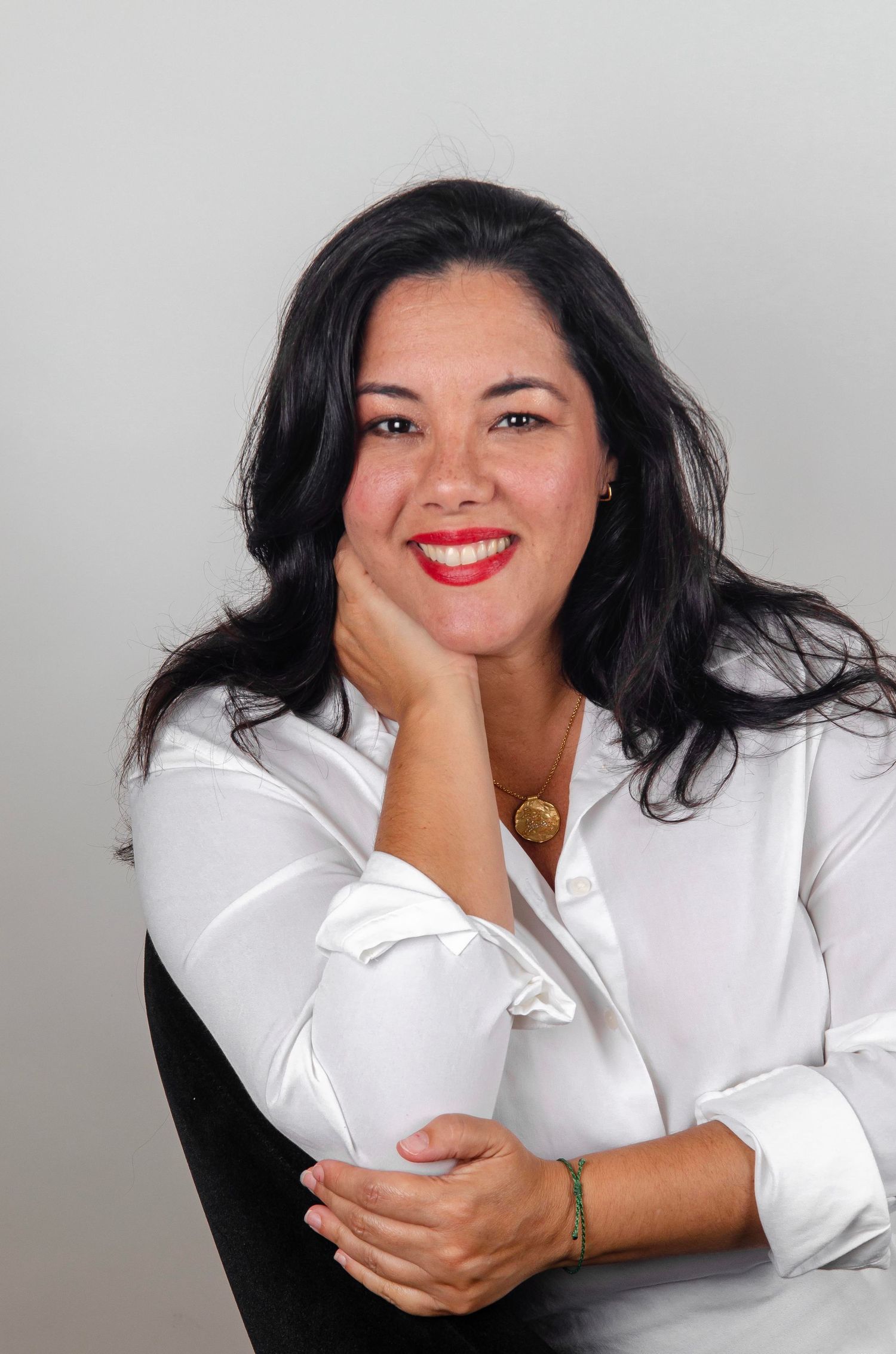 A professional headshot of a person in white blouse against a grey background.