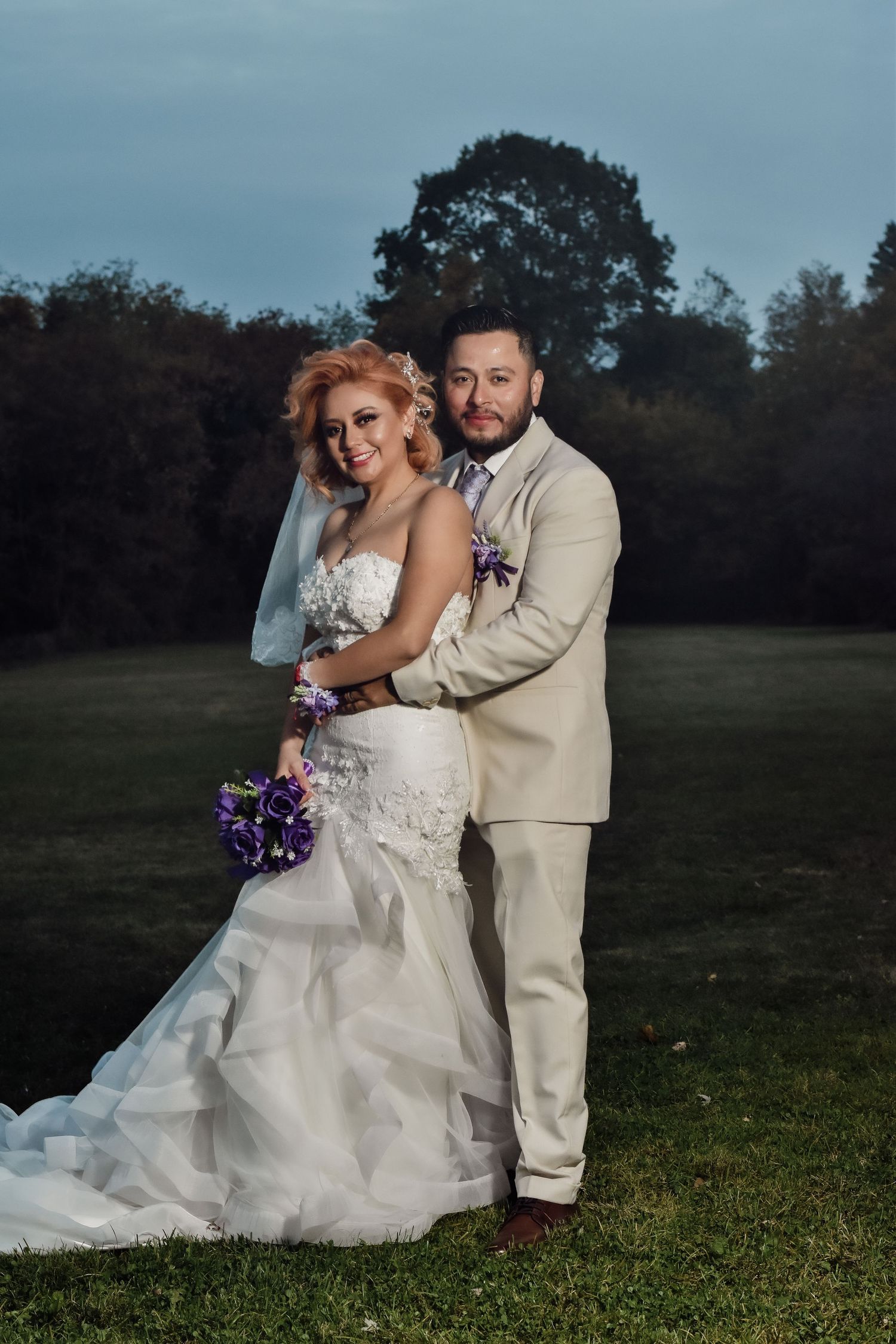 Bride in white mermaid gown holding purple bouquet poses with groom in tan suit outdoors. Toronto GTA