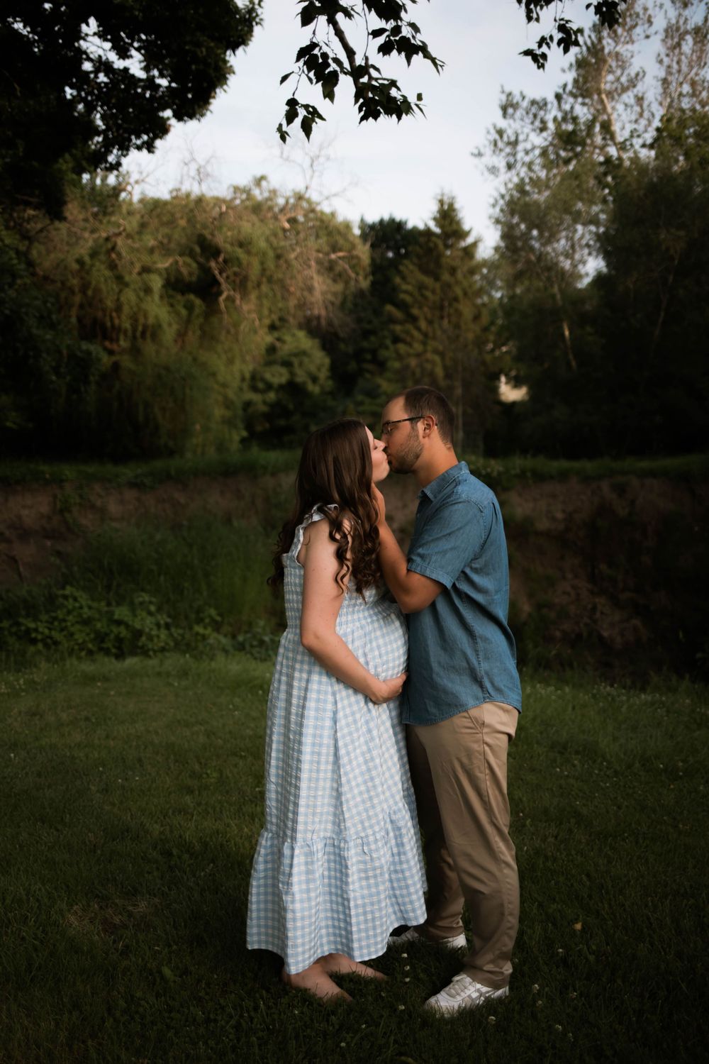 A couple in blue gingham dress and denim embraces in a green outdoor setting.