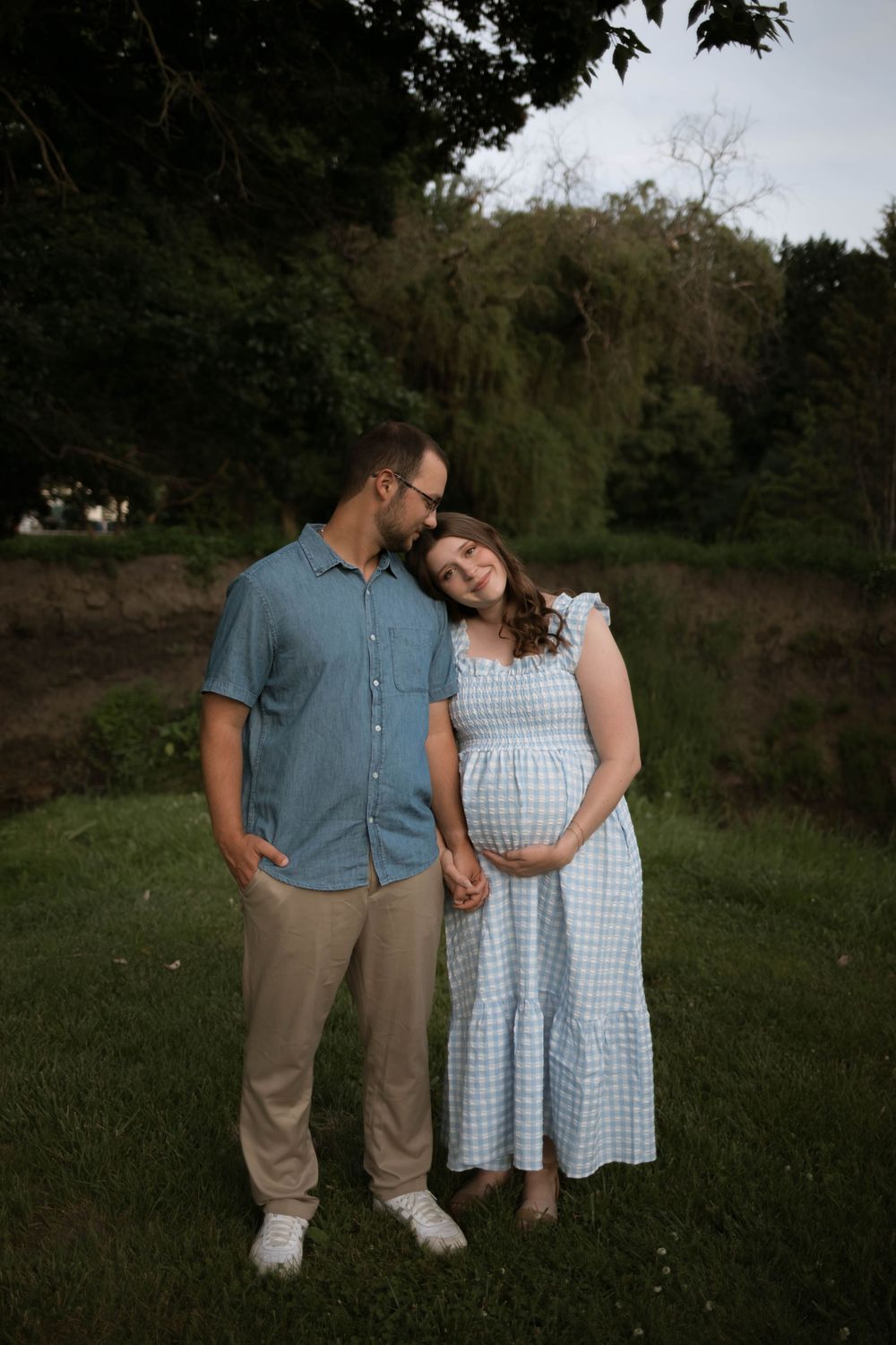 A tender moment between a couple in a park with trees in the background.