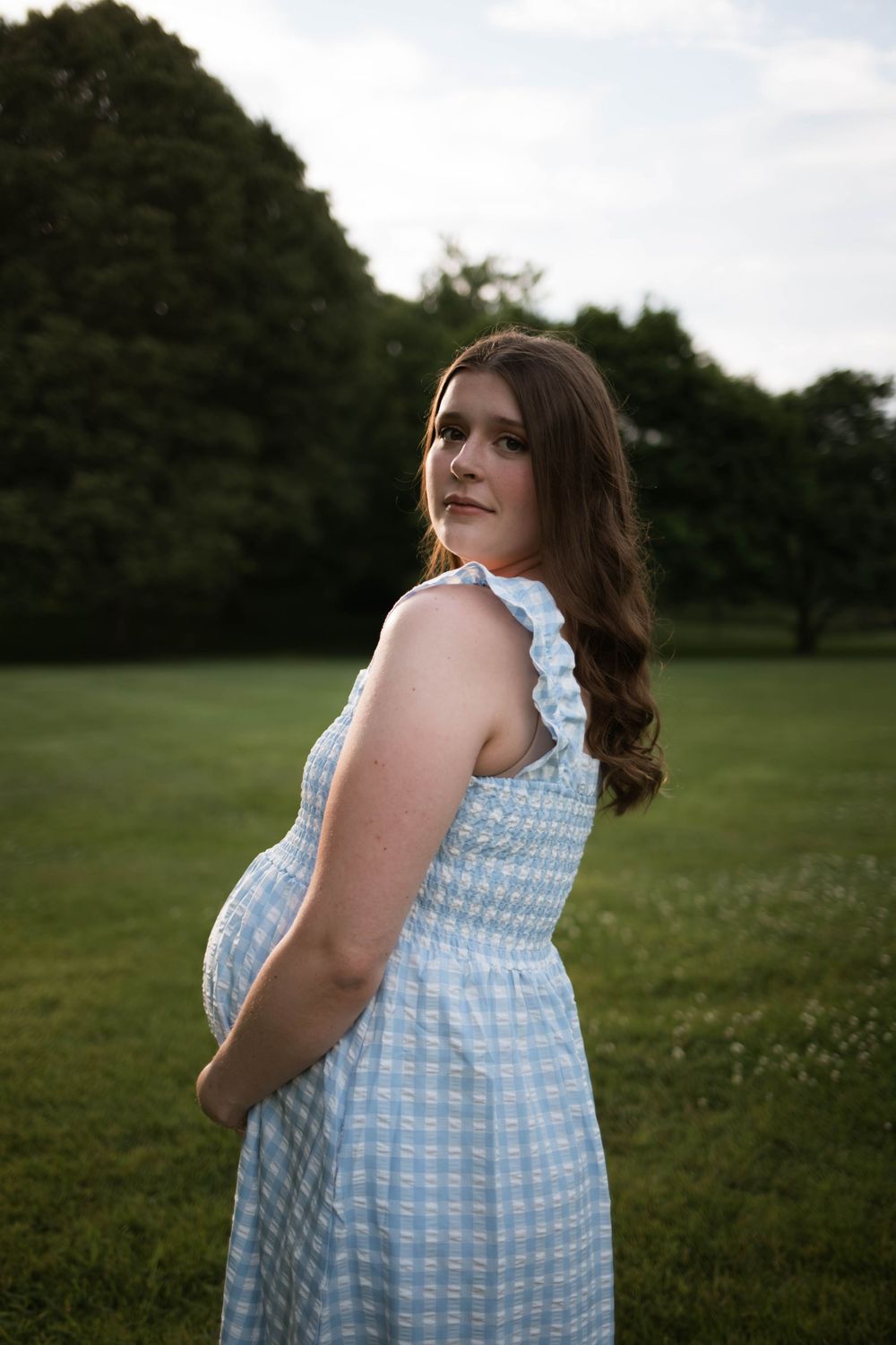A person in a blue gingham dress poses in a sunlit meadow.