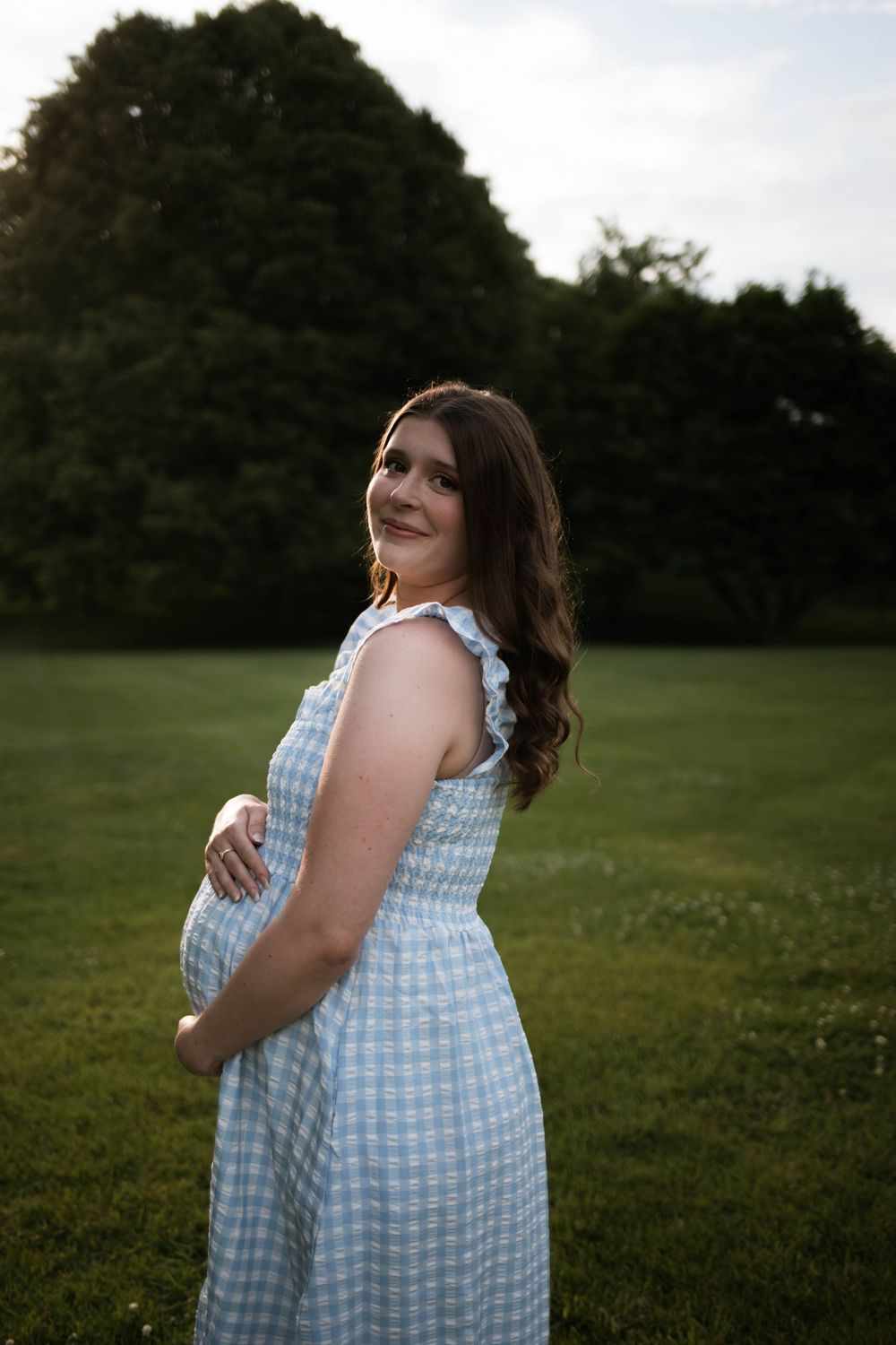 A side view of someone wearing a blue checkered dress in a grassy field.
