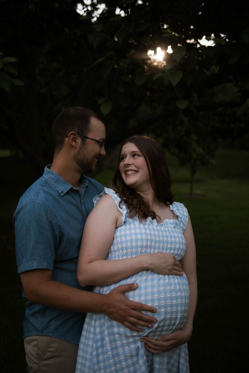 A couple shares a tender moment in evening light while expecting.