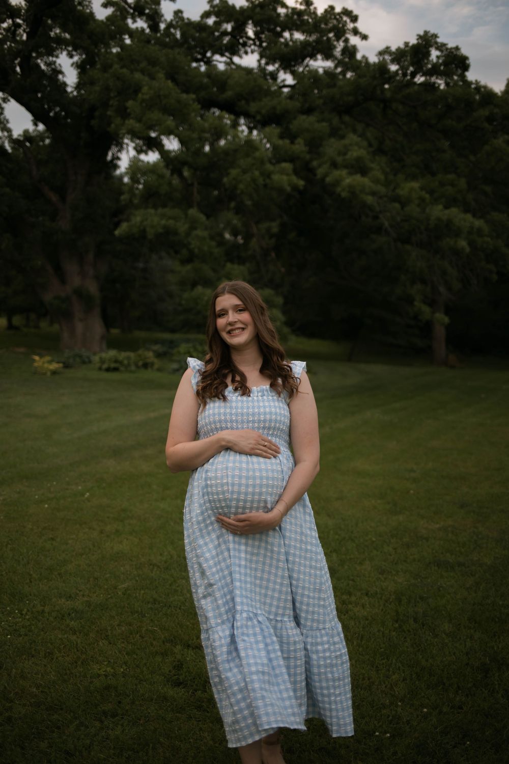 Woman in blue gingham dress stands in a grassy field during golden hour.