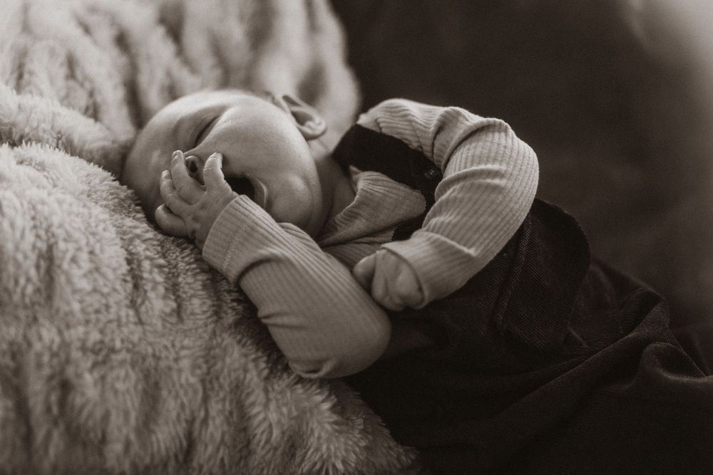 A sleeping infant rests peacefully on soft white bedding in moody lighting.