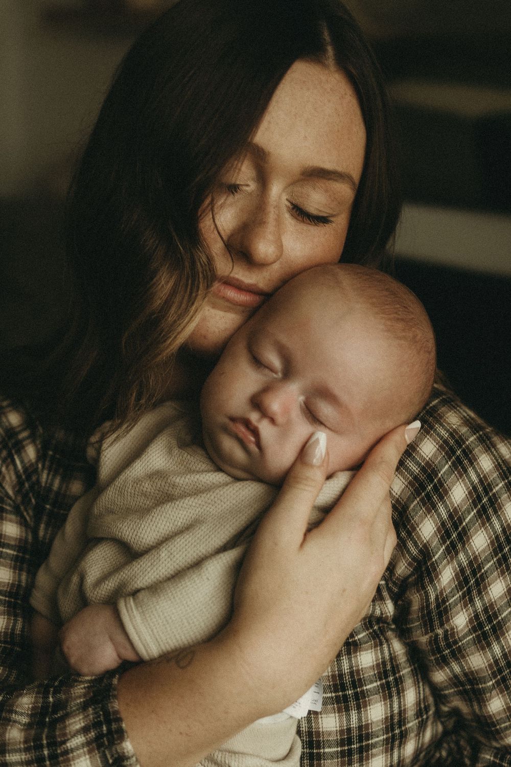 Tender moment between parent and infant in warm, moody lighting.