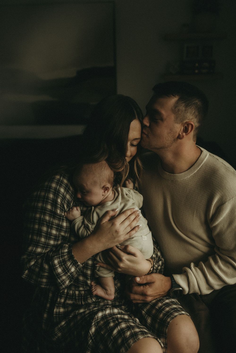 Intimate family portrait in moody lighting with plaid shirt and cream sweater.
