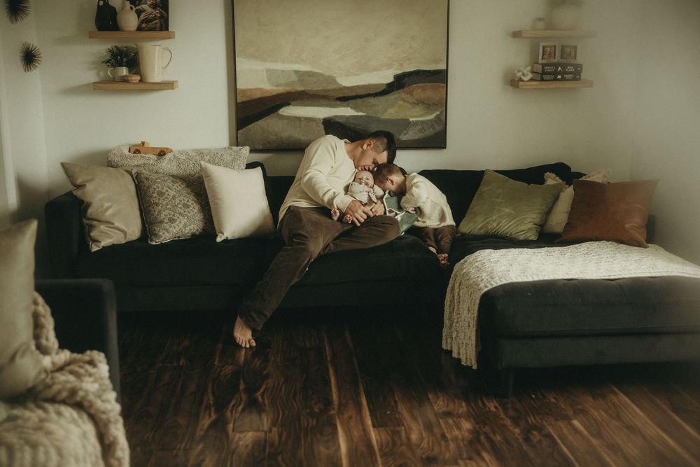 Family relaxing together on a sectional couch with wall art and floating shelves.