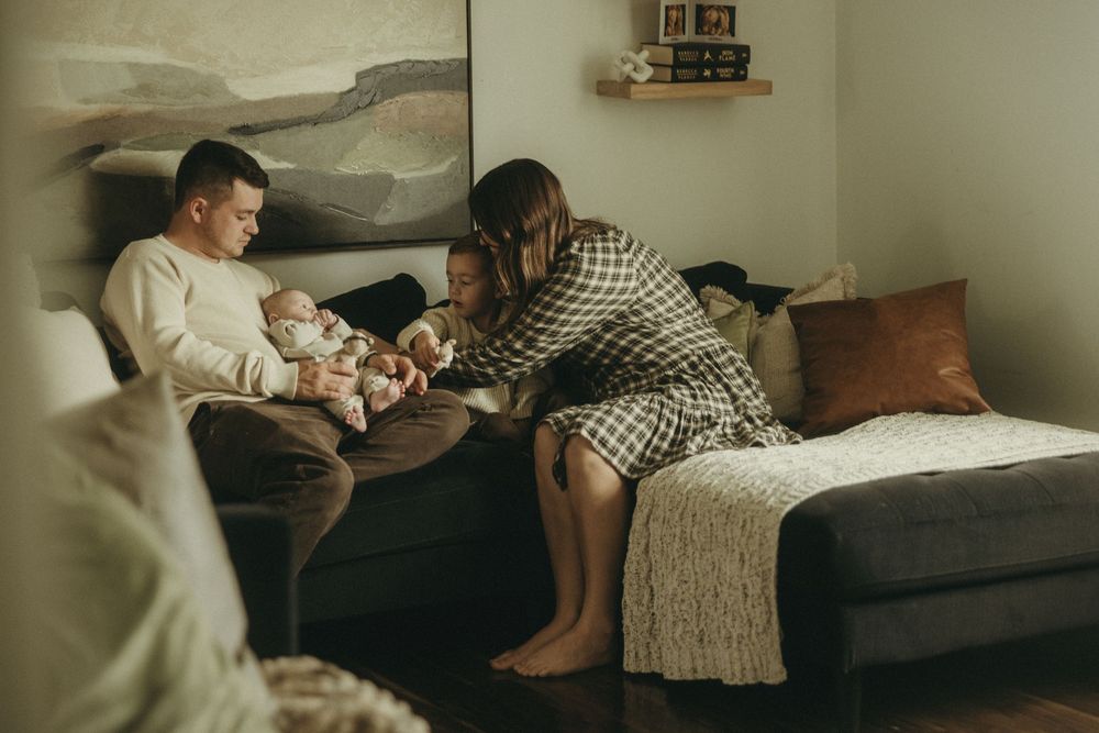 Intimate family moment on dark sectional couch with landscape painting in background.