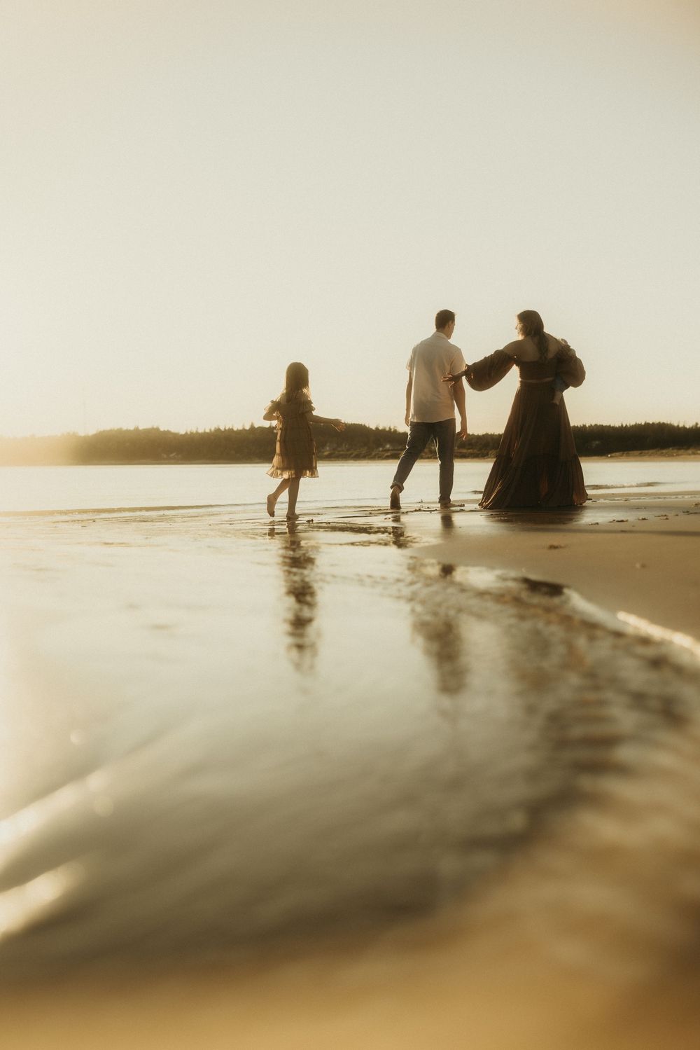 A family walks along the beach shoreline at sunset creating silhouettes against the golden sky.