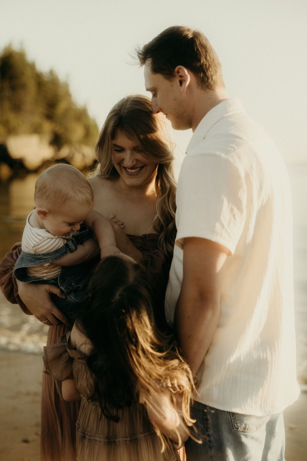 A family and their black dog share joyful moments on the beach at sunset.
