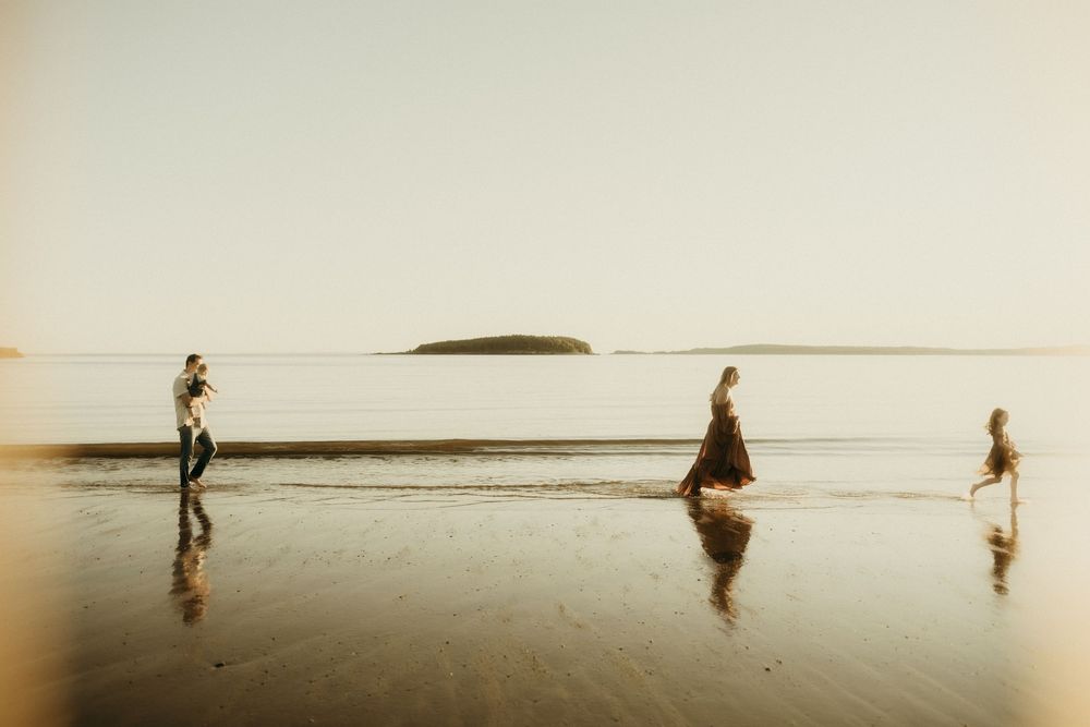 Three silhouettes reflect in wet sand during a peaceful beach sunset.